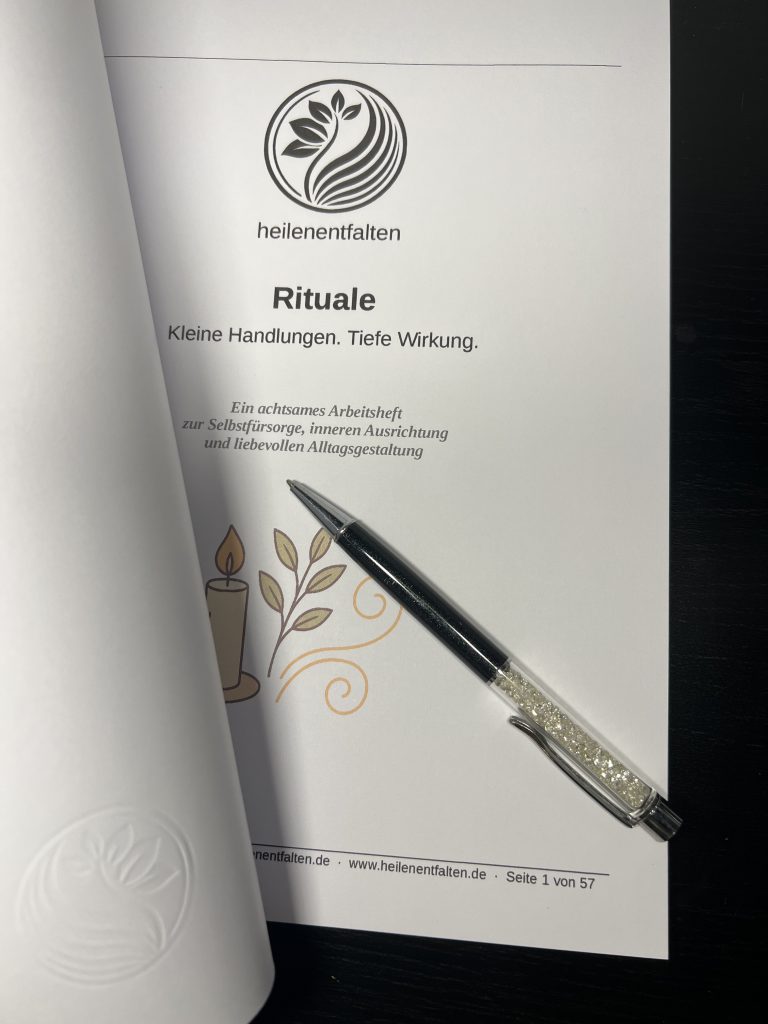 Aufgeschlagenes Arbeitsheft „Rituale“ mit geprägtem Umschlag, sichtbarer Titelseite und Stift auf dunklem Hintergrund